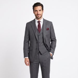 Modelo de frente vistiendo un traje de tres piezas gris marengo para hombre de Sastrería Elías, con americana abrochada, chaleco a juego, camisa blanca, corbata de seda granate y pañuelo de bolsillo burdeos, sobre fondo blanco.